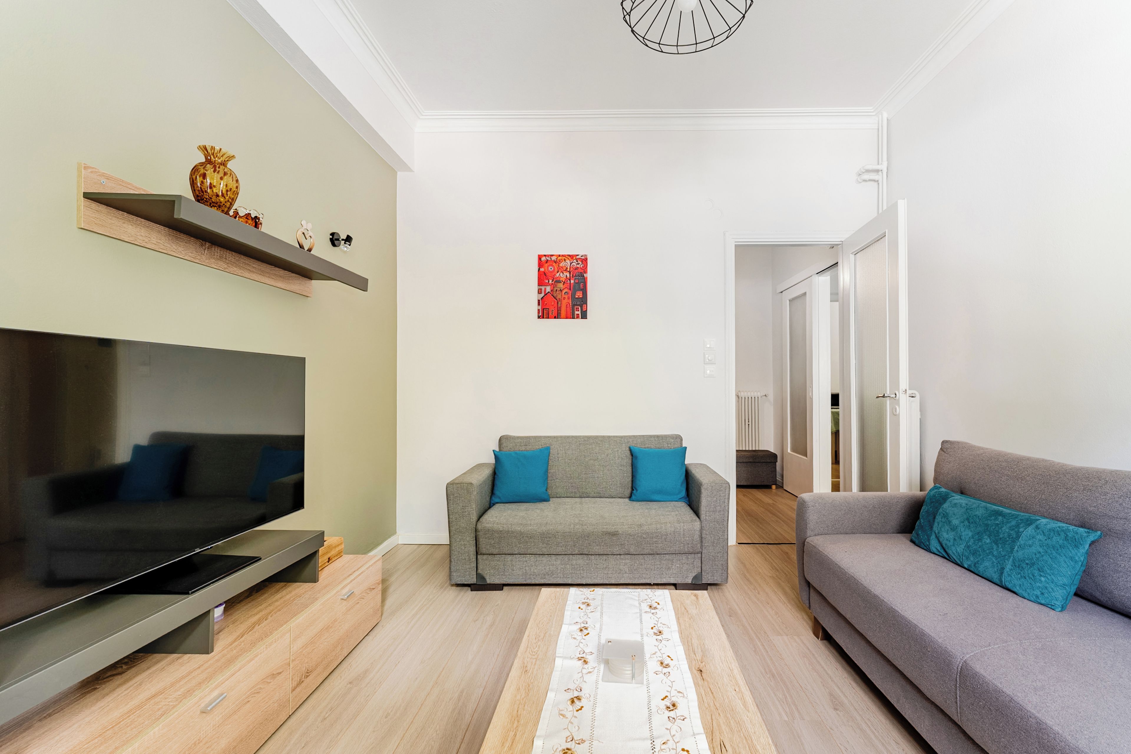 A modern living room with a flat-screen TV, grey sofas, and a decorative rug.