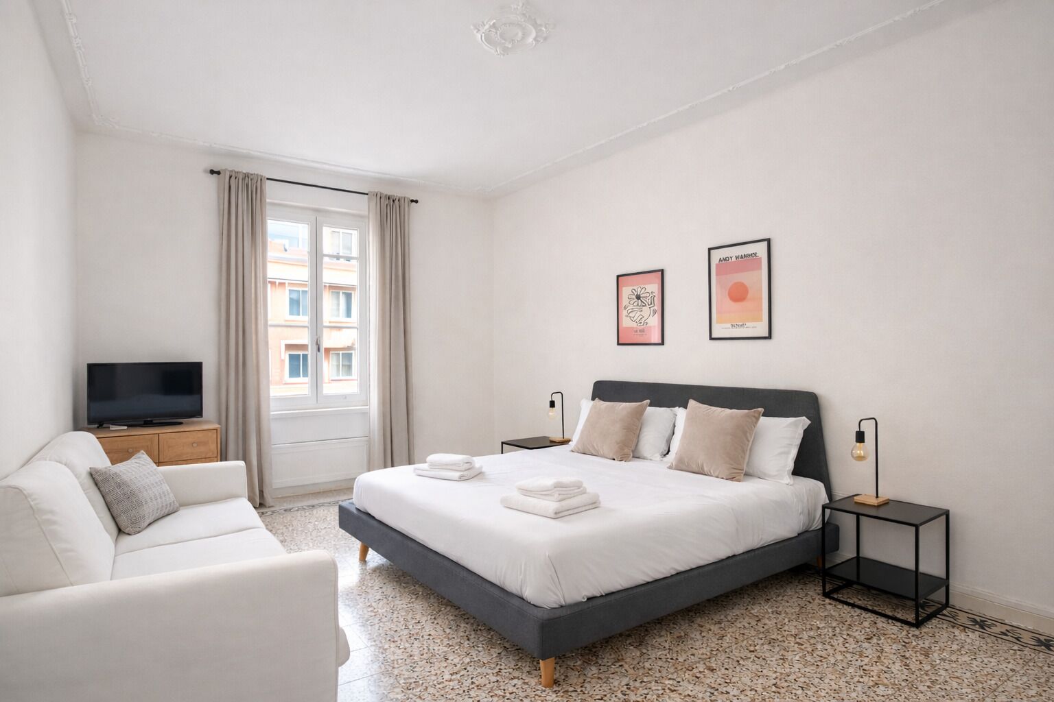 Ein modernes Hotelzimmer mit einem großen Bett, einem Fernseher, einer Couch und Kunstwerken an den Wänden.