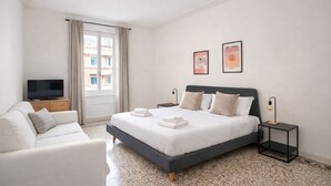 Ein modernes Hotelzimmer mit einem großen Bett, einem Fernseher, einer Couch und Kunstwerken an den Wänden.