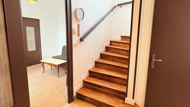 A staircase with wooden steps and a metal handrail, leading to a second floor.