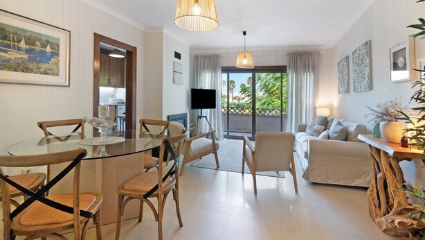 A modern living room with a glass dining table, wooden chairs, a sofa, and a television. - Apartment 'Do Vale Holidays' with Shared Pool, Wi-Fi and Air Conditioning (Guia)