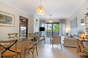 Een moderne woonkamer met een glazen eettafel, houten stoelen, een bank en een televisie.