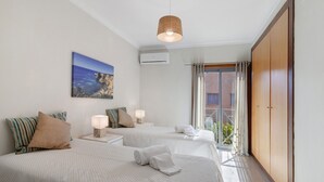 A hotel room with two beds, a large window, a wall-mounted air conditioner, and a hanging light fixture. - Apartment 'Do Vale Holidays' with Shared Pool, Wi-Fi and Air Conditioning (Guia)