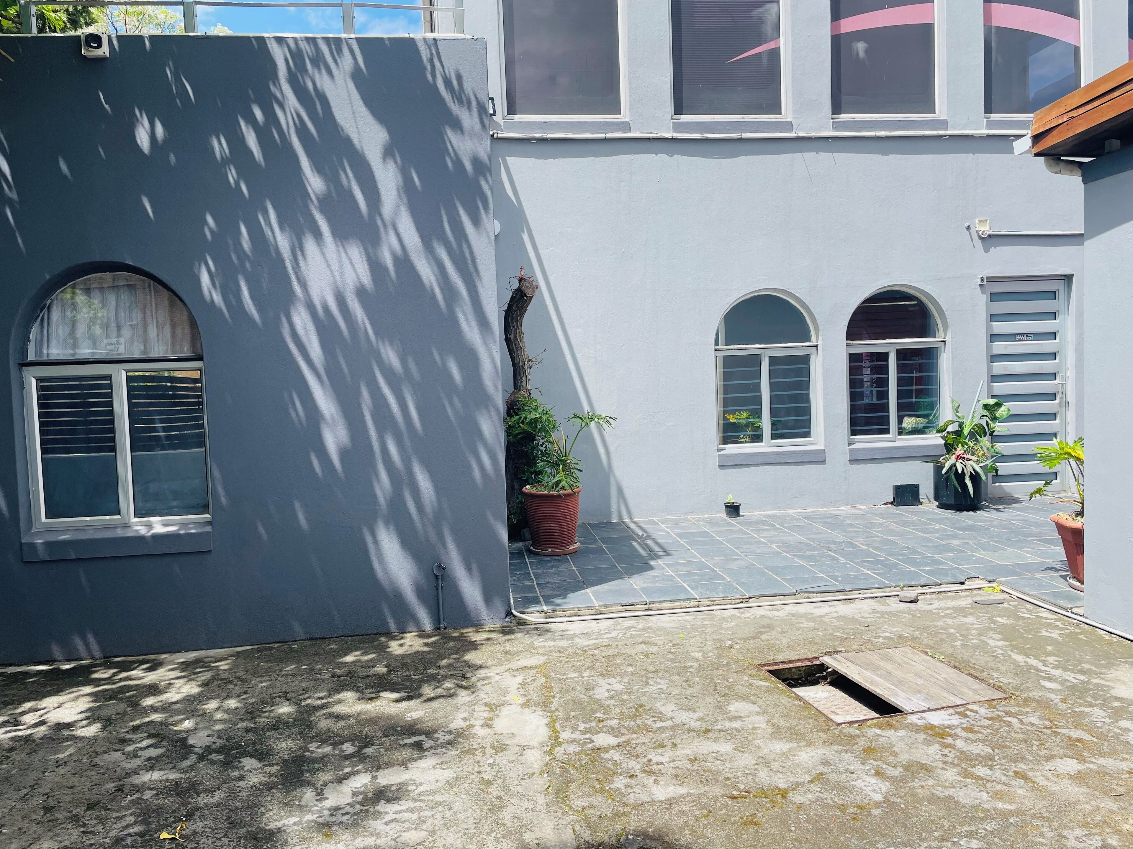 A courtyard with a tiled floor, potted plants, and a small drainage grate.