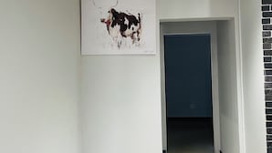 Un pasillo con pared blanca, una lámpara en el techo y una puerta que da a otra habitación.
