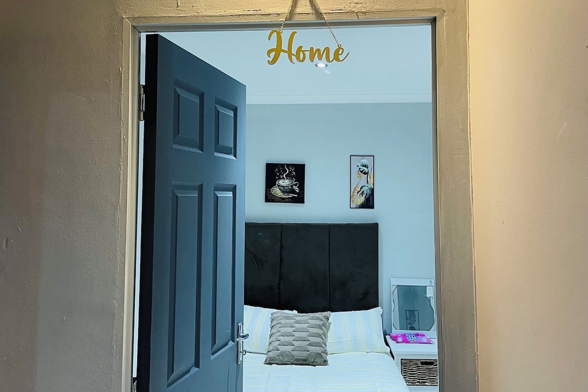 A bedroom with a bed, a bedside table, a lamp, and a wall-mounted light fixture.