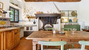 A rustic kitchen with a wooden table, green chairs, and a traditional stove.