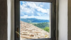 A window with a view of a stone terrace and distant mountains.