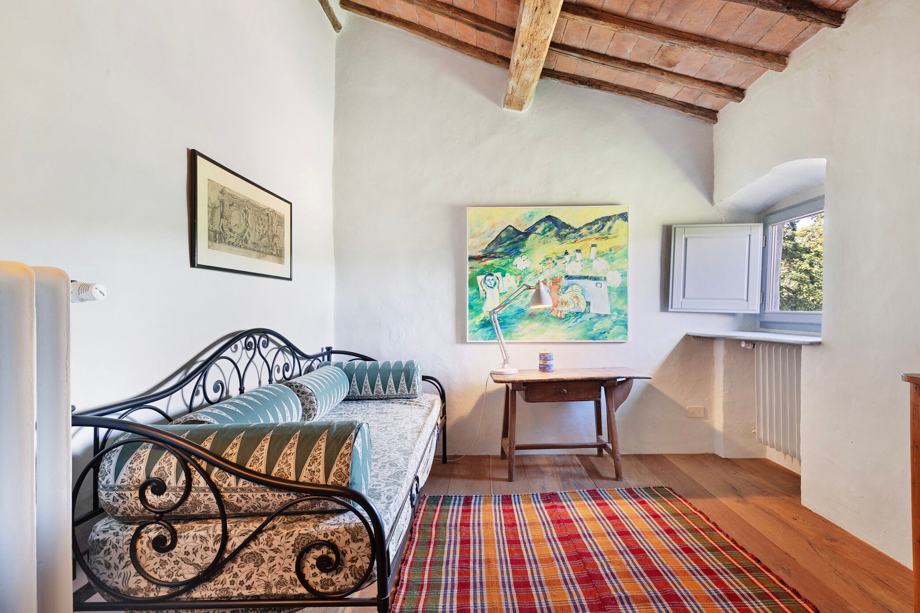 Una habitación con cama, mesa, cuadro y ventana.