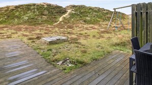 A wooden deck with a swing set and a chair, overlooking a grassy area with a dirt path leading up a hill. - "Asel" - 1km from the sea by Interhome (Fanø)