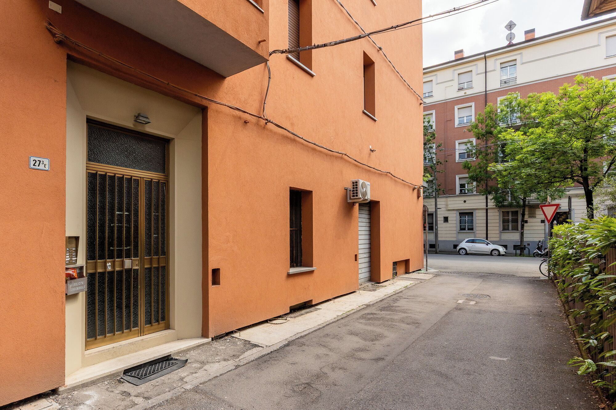 A narrow street with a building featuring a large barred window and a small door.