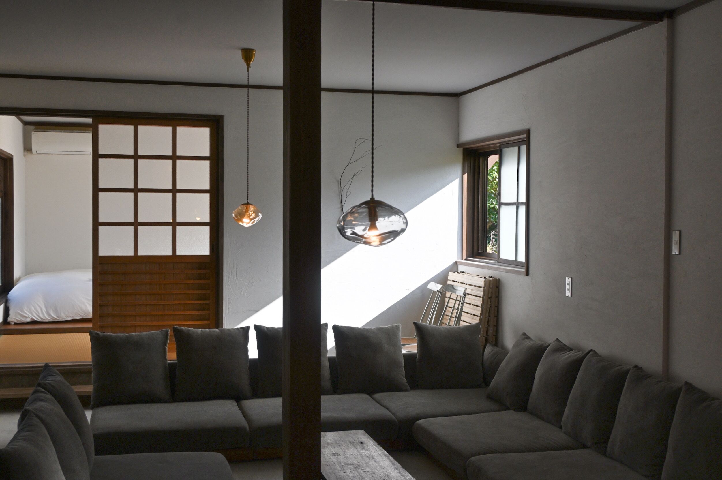 A modern interior with a sofa, a hanging light fixture, and a sliding door leading to a bed.