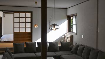 A modern interior with a sofa, a hanging light fixture, and a sliding door leading to a bed.