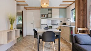 Et kompakt køkken med moderne hårde hvidevarer, et spiseområde med bord og stole, samt en sofa.