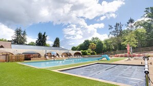 En swimmingpool med parasol, et overdækket siddeområde og en indhegnet legeplads.