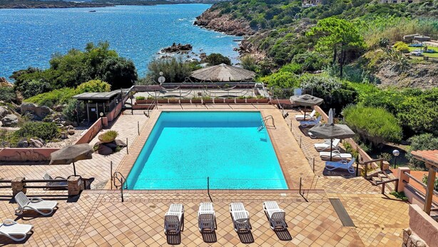 A pool area with lounge chairs and a view of the sea.