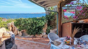 Une terrasse offrant une vue sur la mer, avec une table dressée pour le repas, des chaises en osier et un mur en pierre.
