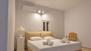A bedroom with a bed, a nightstand, a lamp, a chair, and an air conditioning unit. - Clio Apartment Kea (Otzias)