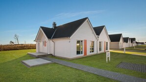 Uma fileira de casas modernas, térreas, com design uniforme, destacando uma entrada central e um pequeno alpendre.