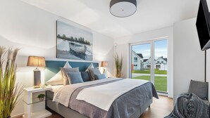 Quarto moderno com uma cama grande, mesas de cabeceira, um quadro e vista para casas pela janela.