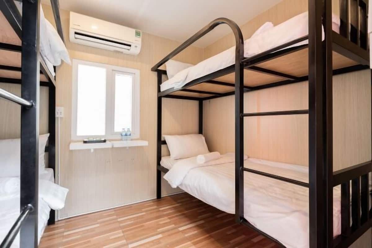 A bunk bed room with a window, wooden flooring, and an air conditioning unit.
