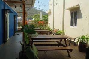 A covered outdoor area with wooden benches, potted plants, and a view of a mountain. - Nin Garden Homestay (Vung Tau)