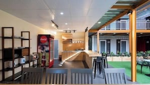 A modern indoor dining area with a long counter, chairs, and a Coca-Cola refrigerator. - Nin Garden Homestay (Vung Tau)