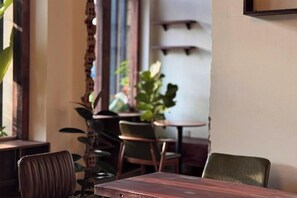 A dining area with tables and chairs, a plant, and a wall with shelves. - Nin Garden Homestay (Vung Tau)