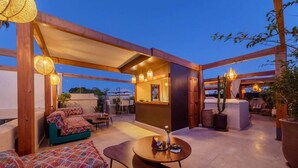 A rooftop terrace with a wooden pergola, a bar area, seating arrangements, and potted plants. - Entire Medina Riad with Rooftop & pool (Marrakesh)