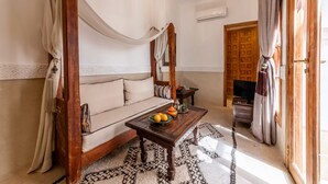 A room with a wooden sofa, a coffee table with fruits, a TV, and a patterned rug. - Entire Medina Riad with Rooftop & pool (Marrakesh)