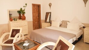 Une chambre à coucher avec un lit, une commode, un miroir, une petite table et une porte.
