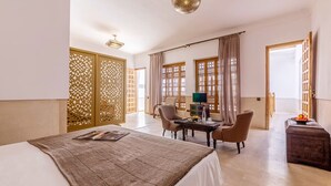 A hotel room with a bed, a dining table with chairs, a TV, and a decorative screen. - Large suite ideal for families (Marrakesh)