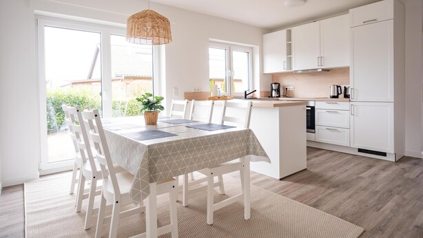 A modern kitchen with white cabinets, a dining area with a table and chairs, and a view of the outdoors.