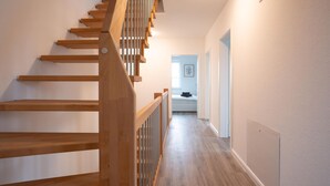 A wooden staircase with a handrail leading to a landing. A hallway with a light-colored floor and walls extends from the staircase. - Spacious holiday and worker accommodation Michelhuus 4 for up to 6 people (Sankt Michaelisdonn)