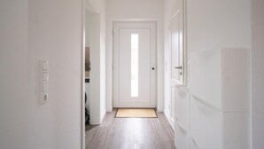 A narrow hallway with a white door at the end, a doormat, and a light switch on the wall. - Spacious holiday and worker accommodation Michelhuus 4 for up to 6 people (Sankt Michaelisdonn)