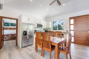 Une cuisine moderne avec des meubles blancs, un réfrigérateur en acier inoxydable, un four à micro-ondes et un coin repas comprenant des chaises et une table en bois.