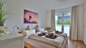 A bedroom with a bed, a desk, a potted plant, a painting, and a view of the outdoors. - Seeblick Nordlicht - Comfortable accommodation on Wangerooge with terrace and garden (Wangerooge)