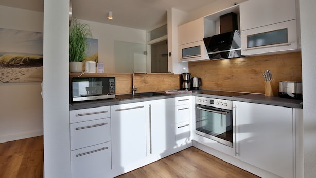 A modern kitchen with white cabinets, a microwave, a coffee maker, and a wooden countertop. - Seeblick Nordlicht - Comfortable accommodation on Wangerooge with terrace and garden (Wangerooge)