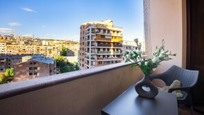 A balcony with a view of a cityscape, a vase with flowers, and a wicker chair.