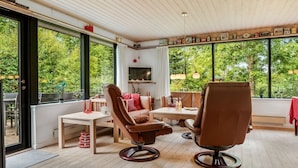 A cozy room with a wooden ceiling, large windows, a sofa, a table, and chairs.
