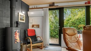 A cozy room with a wood-burning stove, a comfortable leather chair, and a view of greenery outside.
