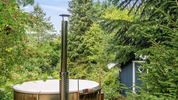A hot tub in a lush garden with dense foliage and a wooden deck.