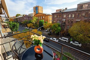 A balcony with a vase of flowers, overlooking a street with cars and buildings. - Apartment by Luxe Group AM104 (Yerevan)