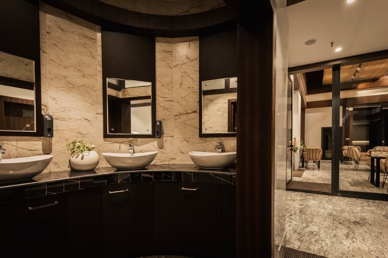 A modern bathroom with three large sinks, marble walls, and a glass door leading to a dining area.