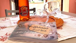 Une table avec une bouteille d’apéritif, deux verres et un livre de bienvenue, le tout posé sur une nappe à motifs évoquant le bord de mer.