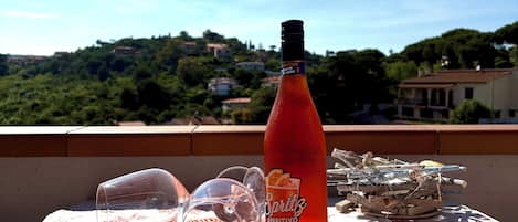 A bottle of Aperitivo on a table with a clear glass and a straw on a woven mat.