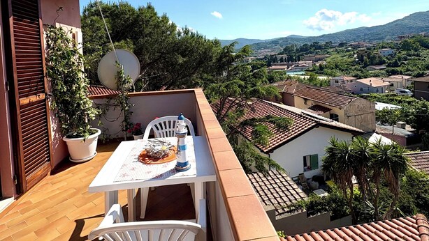 Un balcon avec une table et des chaises, offrant une vue panoramique sur une ville aux toits de tuiles et à la végétation luxuriante.