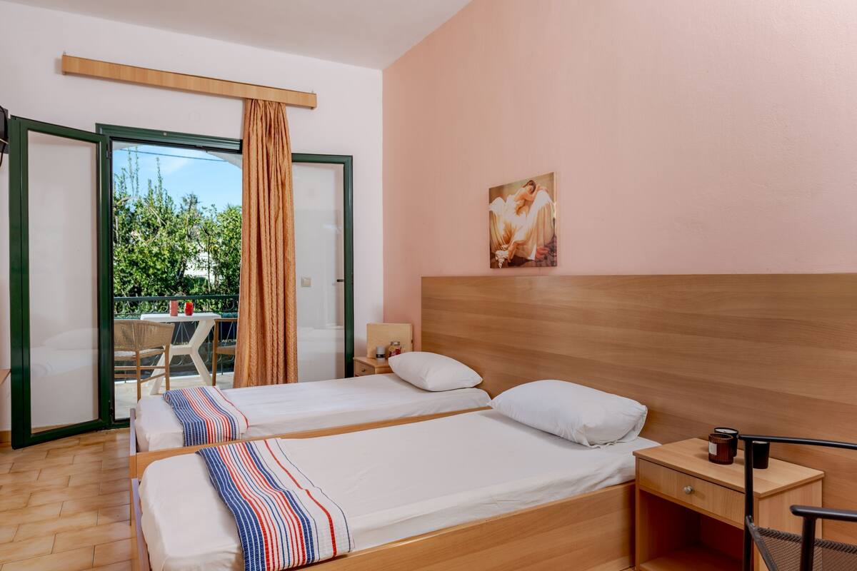 A hotel room with two beds, a wooden headboard, a nightstand, and a view of the outdoors.