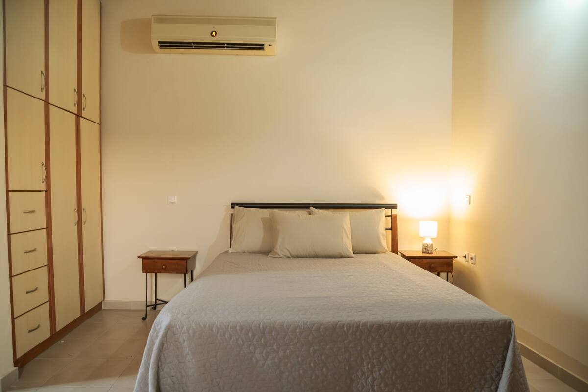 A bedroom with a bed, bedside tables, a wardrobe, and an air conditioning unit.