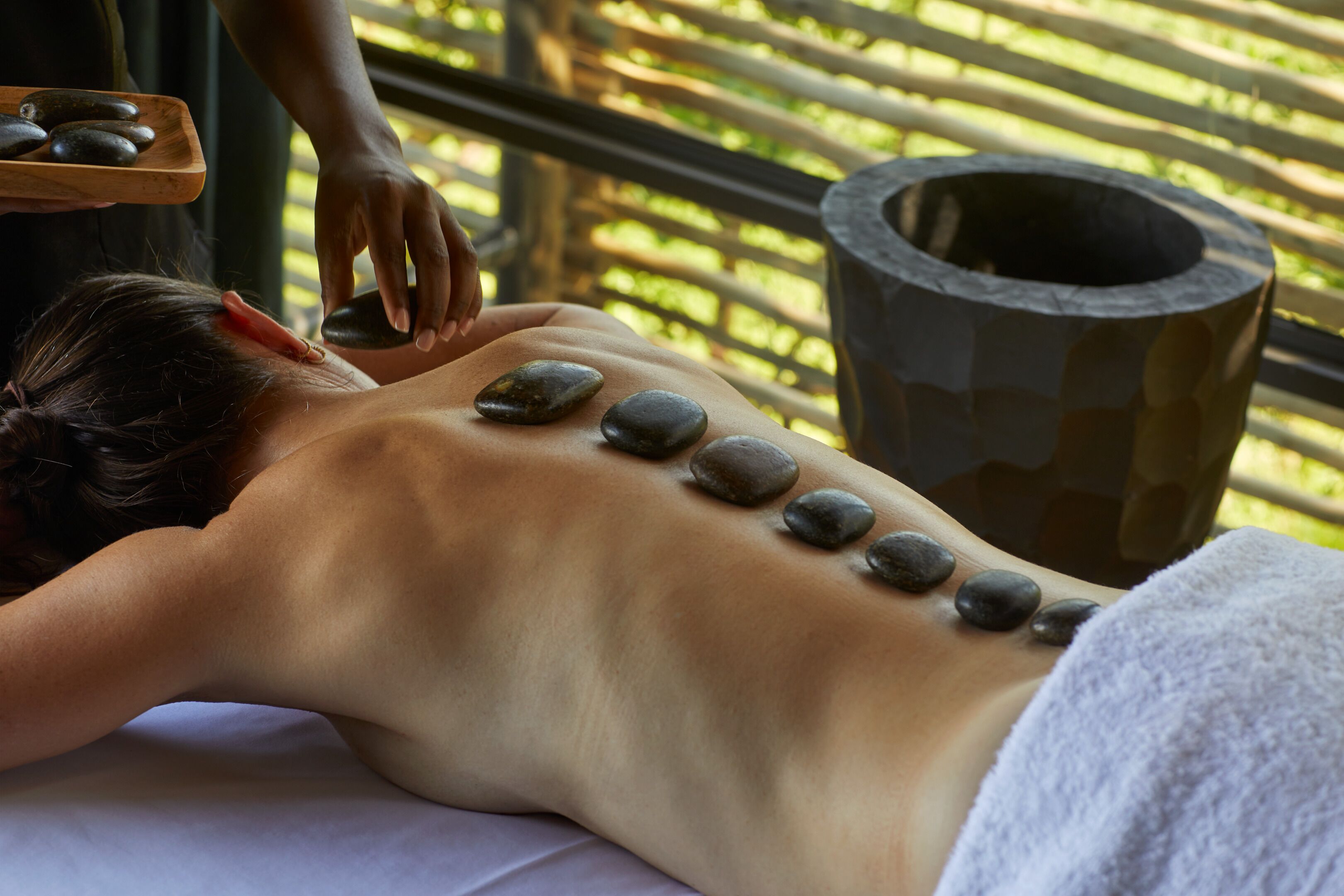 A person receiving a stone massage with a tray of stones and a stone container in the background.